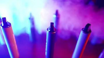 Lots of E-cigarettes and Vapes in Neon Lighting and Smoke. Concept of Bad Habits. Modern Alternative to Tobacco Products. Nicotine Addiction. Slow Motion. video