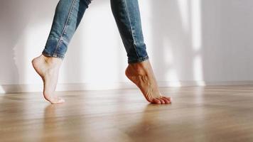 pés descalços femininos bonitos caminham ao longo do piso em parquet da casa sob o sol. câmera lenta. video