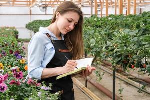 Young woman making notes in a notebook while working in an industrial greenhouse photo