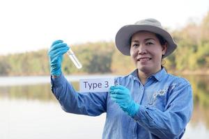 una ecologista asiática sostiene un tubo de agua de muestra y etiqueta con la palabra tipo 3 para inspeccionar e investigar la calidad del agua en el lago. concepto, exploración, análisis de la calidad del agua de fuente natural. campo de la ecología foto