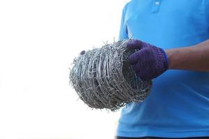 Closeup worker hand holds roll of barbed wire. Concept, construction tool. Barbed wire is used for make fences , secure property ,make border to show the territory of  area. photo