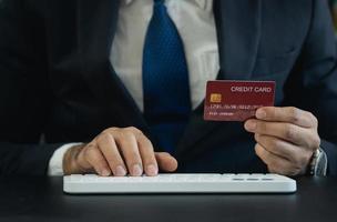 hombre de negocios vestido con traje y con tarjeta de crédito y usando una computadora con teclado para comprar en línea. hombre asiático trabajando en casa. compras en línea, comercio electrónico, banca por Internet, gastar dinero. foto