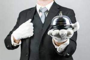 Portrait of Butler or Hotel Concierge Holding Silver Bell. At Your Service Concept. Professional Hospitality. photo