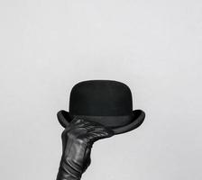 Isolated Leather Glove Hand Holding Bowler Hat on White Background. Concept of British Butler or English Gentleman. photo