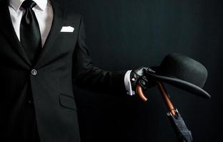 retrato de un hombre de negocios británico con traje oscuro sosteniendo un paraguas y un bombín. estilo vintage de elegante caballero inglés. foto