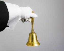 imagen aislada de una mano enguantada blanca sosteniendo una campana de oro sobre fondo blanco. anillo por concepto de servicio. hospitalidad profesional y elegancia. foto