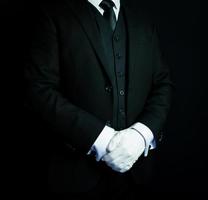 retrato de mayordomo o conserje con traje formal negro y guantes blancos parados en elegante atención. Industria de servicios y hostelería profesional. foto