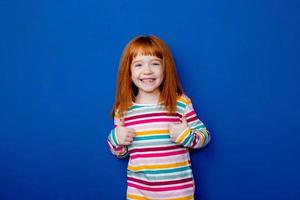 little girl with red hair in a multicolored smile stands on a blue background photo