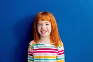 little girl with red hair in a multicolored smile stands on a blue background photo