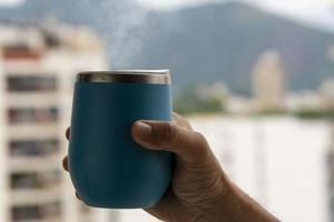 hand holding a coffee mug coming out of smoke with urban environment background photo