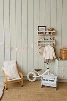 Stylish composition of a cozy Scandinavian interior of a children's room with an armchair, plush and wooden toys, a rattan basket on the chest of drawers and textile hanging flags photo