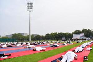 New Delhi, India, June 21 2022 - Group Yoga exercise session for people at Yamuna Sports Complex in Delhi on International Yoga Day, Big group of adults attending yoga class in cricket stadium photo