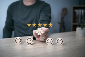 Hand of a businessman chooses a smile face on wood block circle.Customer service experience and business satisfaction survey.rating very impressed.Satisfaction survey concept.five Star Satisfaction photo