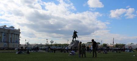 Sankt Petersburg Russia, 06 07 2022 contrast shot of people sitting on grass in Alexander Garden park with silhouette of Bronze Horseman sculpture of Peter the Great on blue sky and sun background photo