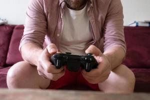 manos con gamepad de hombre sentado en el sofá y jugando videojuegos