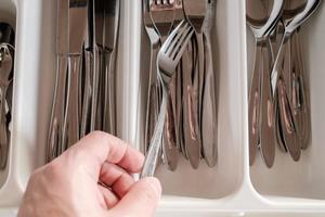 Male hand takes a fork from a drawer with cutlery. Close-up. photo