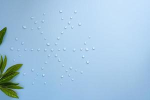 Snowflake from water drops and green leaves on a blue background. Copy space. Flat lay. Top view. photo