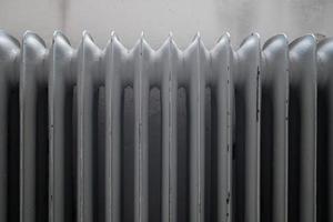 Old cast-iron radiator, painted grey, with peeling paint, against the wall. Close-up. photo