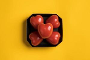 Red tomatoes in the form of a heart in a black cardboard box, on a yellow background. Healthy food concept. Top view.