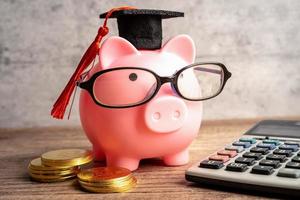 pigging bank usando anteojos con monedas y sombrero de graduación concepto de educación bancaria de ahorro. foto