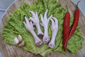 patas de pollo crudas en una tabla de cortar con lechuga, chiles rojos y ajos. patas de pollo frescas y orgánicas. vista superior foto