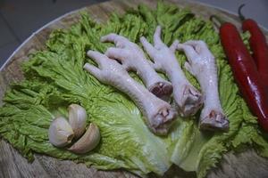 patas de pollo crudas en una tabla de cortar con lechuga, chiles rojos y ajos. patas de pollo frescas y orgánicas. vista superior foto