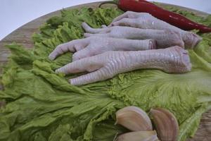 Raw chicken feet on a chopping Board with lettuce, red chilies, and garlics. Fresh and organic chicken feet. Top view photo