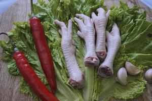 patas de pollo crudas en una tabla de cortar con lechuga, chiles rojos y ajos. patas de pollo frescas y orgánicas. vista superior foto