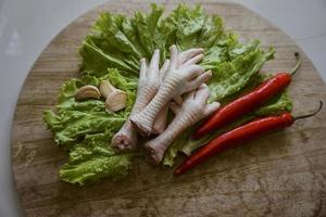 patas de pollo crudas en una tabla de cortar con lechuga, chiles rojos y ajos. patas de pollo frescas y orgánicas. vista superior foto