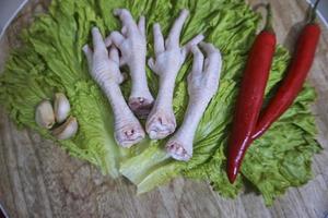 patas de pollo crudas en una tabla de cortar con lechuga, chiles rojos y ajos. patas de pollo frescas y orgánicas. vista superior foto