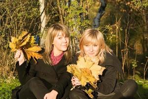dos mujeres jóvenes con hojas de otoño en el parque foto