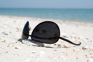 las gafas de sol negras tiradas en una playa foto