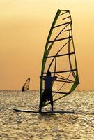 Silhouettes of a windsurfers on waves of a bay photo