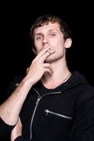 The young man smokes a cigarette. Isolated on a black background photo