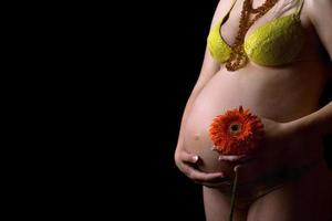 Belly of a pregnant young woman with flower. Isolated photo