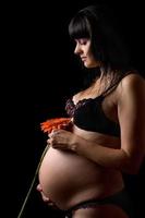 Pregnant young brunette with red flower. Isolated photo