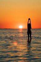 silueta de la joven con las manos hacia arriba en una bahía al atardecer foto