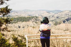 Back view blue hair caucasian woman hold smartphone take photo of beautiful nature outdoors on holiday vacation. Use different photo modes on screen tap record capture button