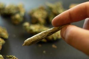 mano con articulación de marihuana, fondo borroso con cogollos de cannabis. uso de drogas médicas de hierba para el autocuidado. thc legal para el concepto de recreación foto