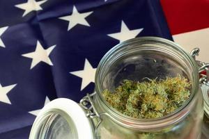 gran tarro de vidrio de cogollos de hierba con fondo de bandera nacional de estados unidos. primer plano de cannabis con espacio de copia foto