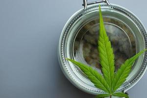 Marijuana leaf on glass jar top view. Cannabis legal industry. Weed use in medicine and healthcare. Copy space background photo