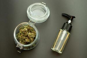 aceite de hierbas cbd con brotes de cannabis en la vista superior del frasco de vidrio. marihuana sobre fondo negro. concepto de industria de negocios de malezas. uso médico y recreativo de la atención sanitaria del cannabidiol foto