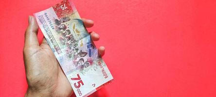 hombre con billete de 75.000 rupias indonesias, último número foto