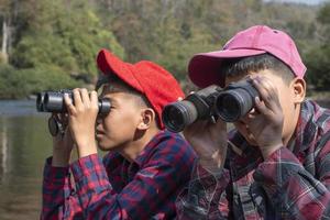 Asian boys are using binoculars to watch birds and fish  in local national park during summer camp, idea for learning creatures and wildlife animals and insects outside the classroom. photo