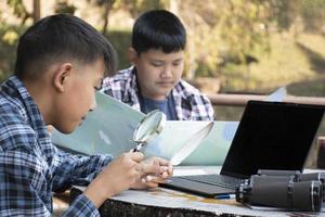 Asian boys using binoculars to watch birds on trees and fish in river in local national park during summer camp, idea for learning creatures and wildlife animals and insects outside the classroom. photo