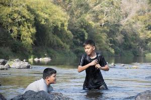Asian boys are spending their freetimes by diving, swimming, throwing rocks and catching fish in the river together happily. Hobby and happiness of children concept. photo