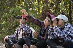 Asian boys using binoculars to watch birds on trees and fish in river in local national park during summer camp, idea for learning creatures and wildlife animals and insects outside the classroom. photo