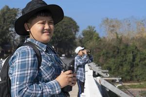 Asian boys using binoculars to watch birds on trees and fish in river in local national park during summer camp, idea for learning creatures and wildlife animals and insects outside the classroom. photo