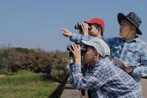 niños asiáticos que usan binoculares para observar pájaros en los árboles y peces en el río en el parque nacional local durante el campamento de verano, idea para aprender criaturas y animales salvajes e insectos fuera del aula. foto