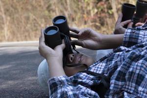 Asian boys using binoculars to watch birds on trees and fish in river in local national park during summer camp, idea for learning creatures and wildlife animals and insects outside the classroom. photo